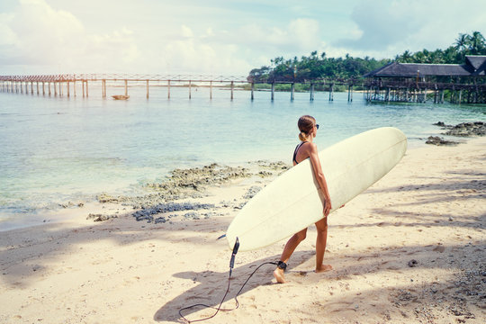 It's time for surfing! Hobby and vacation. Young woman holding surf board on the sea shore.