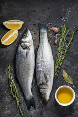 Fresh fish seabass and ingredients for cooking, lemon and rosemary. Dark background top view.