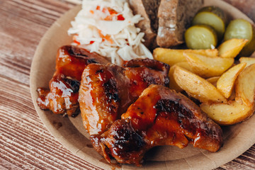 Delicious fried chicken wings with sauce, fried potatoes, cucumber, cabbage and khlobe in a paper plate on a wooden table. takeaway street food