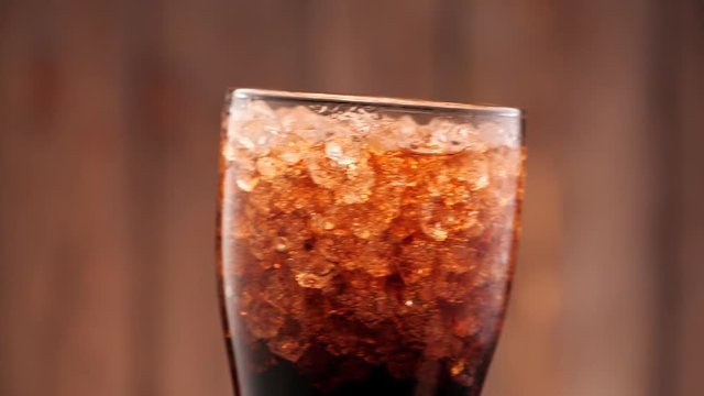 Full glass of cola with ice. Someone puts it in the frame in slow motion.