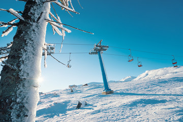 Ski lift with seats going over the mountain and paths from skies and snowboards. Beautiful winter landscape.