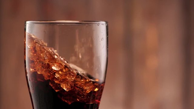 Full glass of cola with ice. Someone puts it in the frame in slow motion.