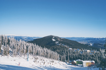 Snowy mountains and ski lifts. Skiers and snowboarders skiing downhill to village.