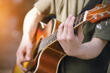 The guy in the green hoodie plays a bright orange acoustic six-string guitar, holding the chords....