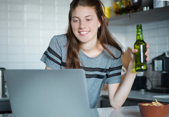 Young woman using laptop with headphones in the kitchen