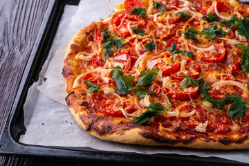 Freshly cooked hot pizza with cheese ham meat tomato onion parsley homemade on parchment paper in baking sheet tray recipe on dark wooden table