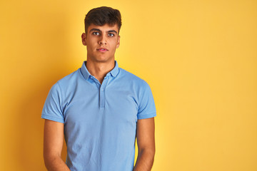 Obraz premium Young indian man wearing blue polo standing over isolated yellow background with serious expression on face. Simple and natural looking at the camera.