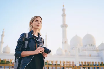 Foto auf Acrylglas Traveling by Unated Arabic Emirates. Pretty Young Woman with camera standing near the Sheikh Zayed Grand Mosque, famous Abu Dhabi sightseeing. © luengo_ua