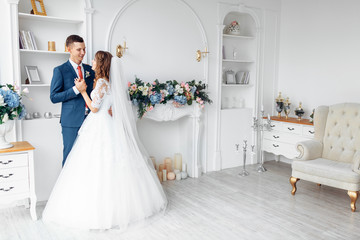 Beautiful bride in white dress and groom in suit, posing in white Studio interior, wedding