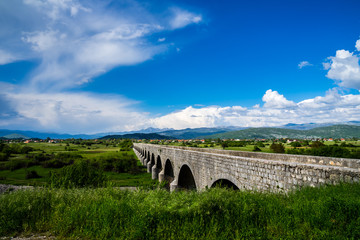 Montenegro, Ancient emperors bridge building architecture of many arches in green beautiful mountain and valley nature landscape of niksic town with blue sky