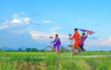 independence Day concept - Two happy young local boy riding old bicycle at paddy field holding a Malaysian flag