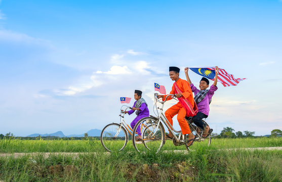 independence Day concept - Two happy young local boy riding old bicycle at paddy field holding a Malaysian flag