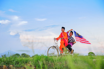 Obraz premium independence Day concept - Two happy young local boy riding old bicycle at paddy field holding a Malaysian flag