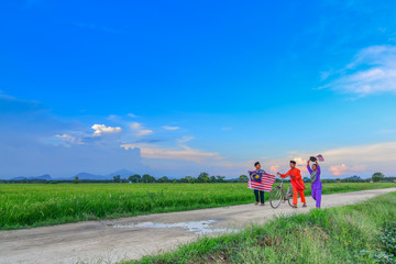 Obraz premium Independence Day concept - Three happy young local boy walking at paddy field holding a Malaysian flag
