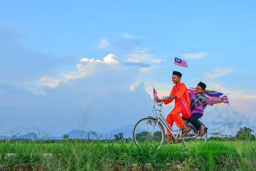 independence Day concept - Two happy young local boy riding old bicycle at paddy field holding a Malaysian flag