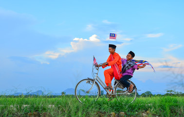 Naklejka premium independence Day concept - Two happy young local boy riding old bicycle at paddy field holding a Malaysian flag