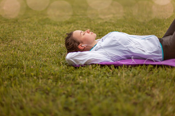 girl in sportswear resting lying on the grass, listening to music after training, jogging, exercising outdoors, urban style, healthy lifestyle