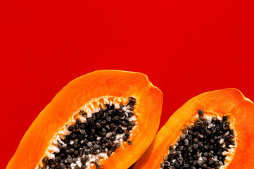 Fresh papaya exotic tropical fruit on red background. Sun day light illumination. Minimalistic summer flat lay wallpaper. Creative food concept. Copy space template.
