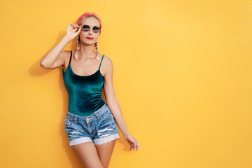 Summer urban fashion. Fun and colorful. Young pretty happy woman in shorts posing against yellow wall.