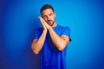 Young handsome man wearing casual t-shirt over blue isolated background sleeping tired dreaming and posing with hands together while smiling with closed eyes.