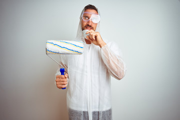 Painter man wearing professional worker equipment holding roller over isolated background serious...