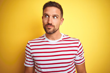 Young handsome man wearing casual red striped t-shirt over yellow isolated background smiling looking to the side and staring away thinking.