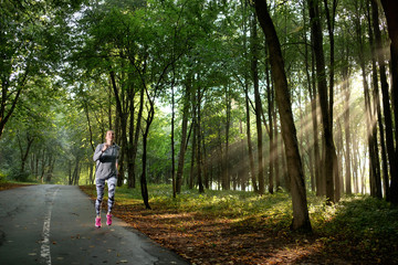Fototapeta na wymiar Athletic young woman wearing sportswear running in the park or forest in sunny morning. Right morning. Summer time.