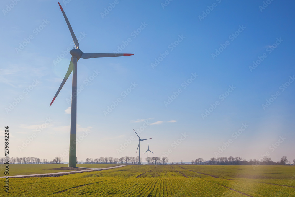 Wall mural wind turbine on green field with sun flare blue sky background