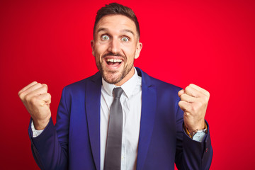 Young handsome business man over red isolated background celebrating surprised and amazed for success with arms raised and open eyes. Winner concept.
