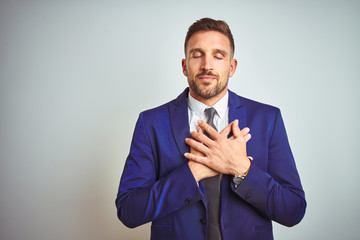 Young handsome business man over white isolated background smiling with hands on chest with closed eyes and grateful gesture on face. Health concept.