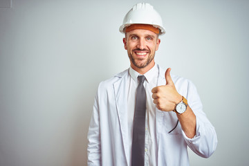 Young handsome engineer man wearing safety helmet over isolated background doing happy thumbs up gesture with hand. Approving expression looking at the camera with showing success.