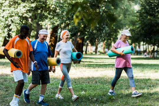 Selective Focus Of Happy Multicultural And Senior Pensioners Walking With Fitness Mats In Park