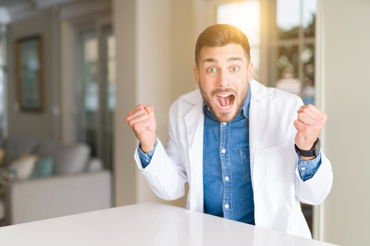 Young handsome doctor man at the clinic celebrating surprised and amazed for success with arms raised and open eyes. Winner concept.
