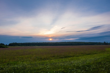 Yellow-orange disk of the setting sun over the horizon and a little cloudy.