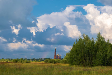 Multicolor rainbow on the background of a beautiful cloudy sky and a red church with a bell tower.