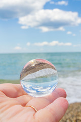 The glass round ball on the hand reflects the beach in the summer