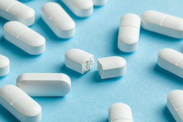 White pills on blue background. One tablet is broken in half, reducing the dose of the medicine