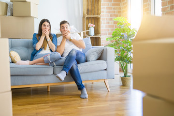 Young beautiful couple relaxing sitting on the sofa around boxes from moving to new house shocked...