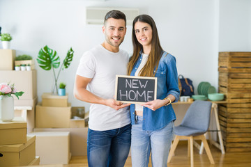 Fototapeta na wymiar Beautiful young couple moving to a new house, smiling very happy holding blackboard with new home text