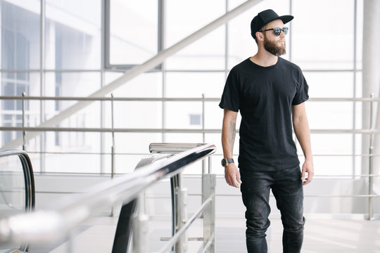 Hipster handsome male model with beard wearing black blank t-shirt with space for your logo or design in casual urban style