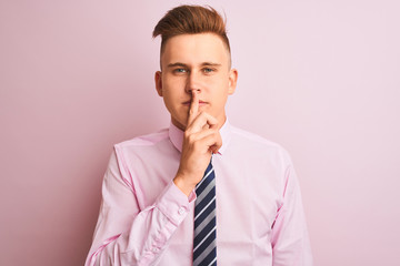 Young handsome businessman wearing shirt and tie standing over isolated pink background asking to be quiet with finger on lips. Silence and secret concept.