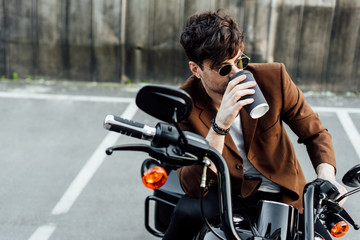 Handsome man in brown jacket drinking coffee from paper cup