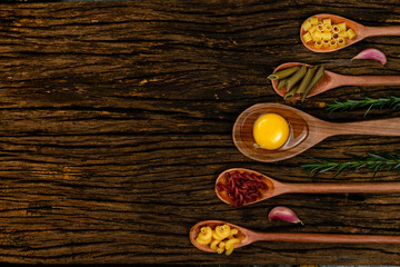 Different pasta types in wooden spoons on the table. Top view. Space for text. Old wooden background.