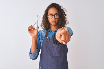 Young brazilian hairdresser woman using scissors standing over isolated white background pointing with finger to the camera and to you, hand sign, positive and confident gesture from the front