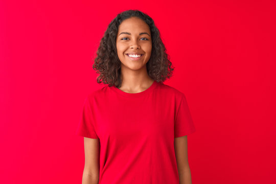 Young brazilian woman wearing t-shirt standing over isolated red background with a happy face standing and smiling with a confident smile showing teeth