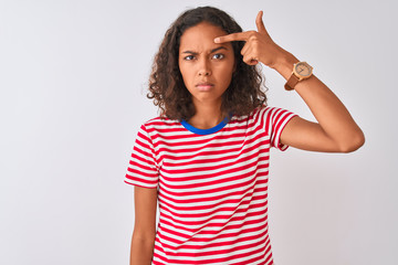 Young brazilian woman wearing red striped t-shirt standing over isolated white background pointing unhappy to pimple on forehead, ugly infection of blackhead. Acne and skin problem