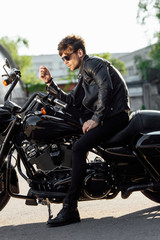 Fototapeta na wymiar side view of motorcyclist in sunglasses and leather jacket sitting on motorcycle