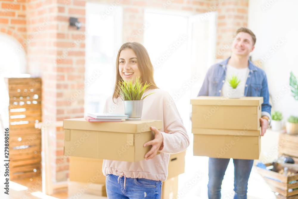 Wall mural beautiful young couple smiling in love holding cardboard boxes, happy for moving to a new home