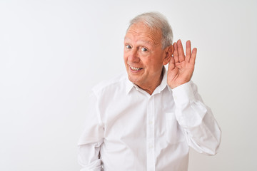 Senior grey-haired man wearing elegant shirt standing over isolated white background smiling with hand over ear listening an hearing to rumor or gossip. Deafness concept.