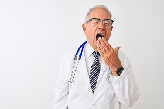 Senior grey-haired doctor man wearing stethoscope standing over isolated white background bored yawning tired covering mouth with hand. Restless and sleepiness.
